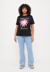Svart T-skjorte med palmestre-grafikk, rosa og gull detaljer, løs passform, kombinert med lyseblå utsvingte jeans og grå joggesko.