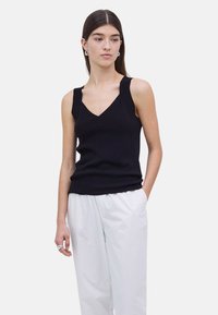 Top negro sin mangas con un diseño de escote en V y tirantes gruesos, hecho de un material suave y acanalado, combinado con pantalones blancos de corte holgado.