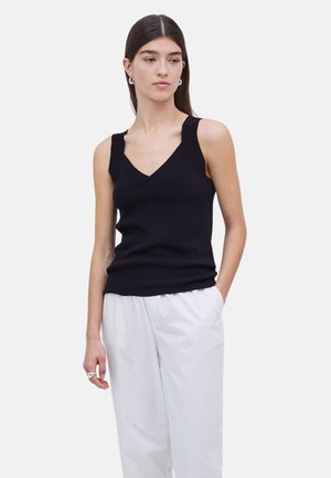 Top negro sin mangas con un diseño de escote en V y tirantes gruesos, hecho de un material suave y acanalado, combinado con pantalones blancos de corte holgado.