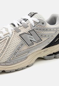 Baskets de course légères avec une empeigne en mesh grise et blanche, présentant un logo gris, des accents superposés et une semelle rembourrée.