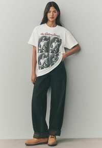 Hvid bomulds t-shirt med The Rolling Stones grafik i sort, parret med løstsiddende sorte jeans og brune snørebåndsstøvler.