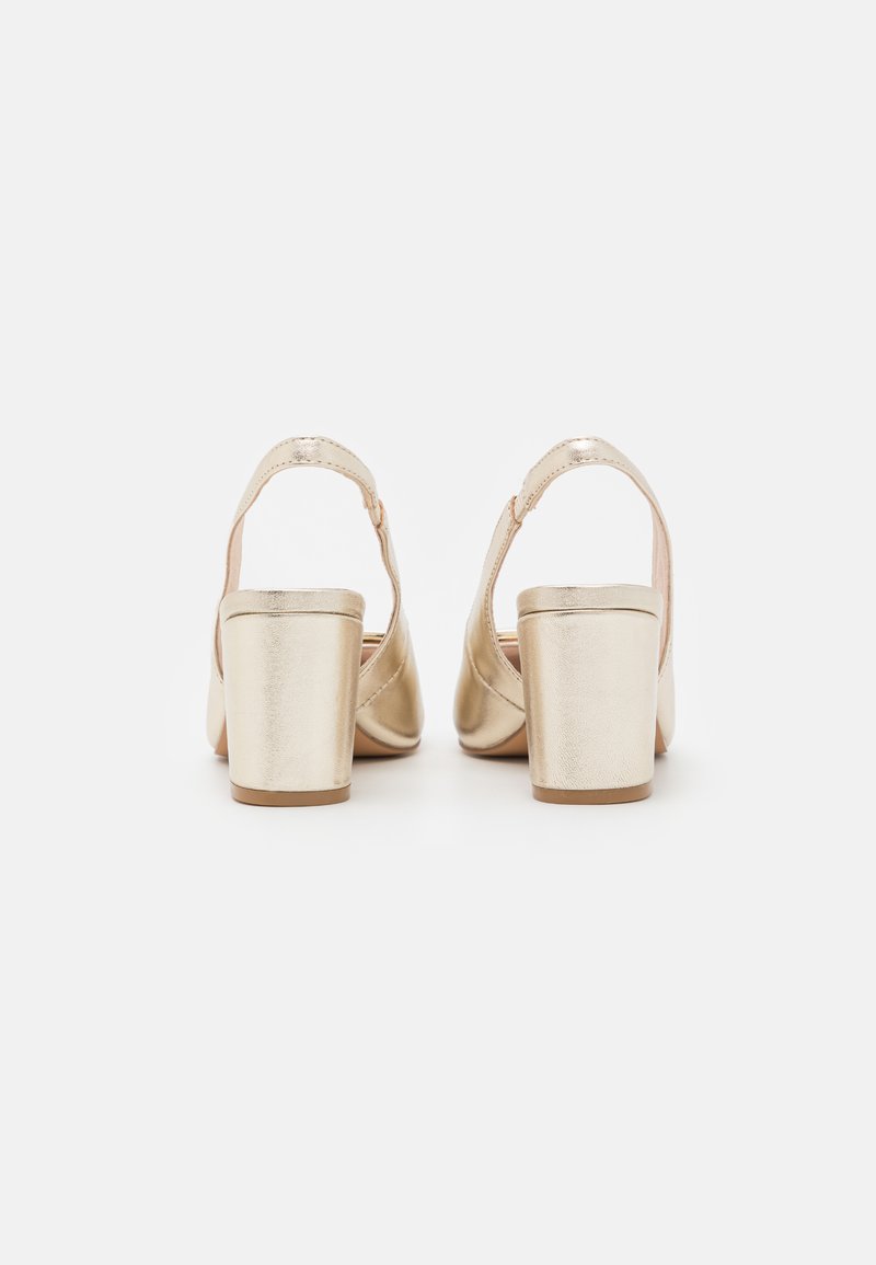 Sandales à talons métalliques dorées avec un design découpé arrondi, des talons blocs épais et une sangle à la cheville arrière. Texture lisse avec une finition brillante.