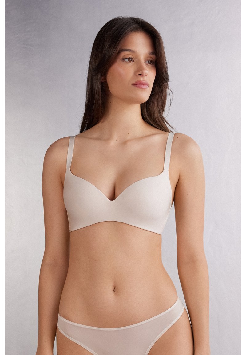 Beige draadloze bh met een diepe V-hals, naadloos ontwerp, gladde textuur en dunne verstelbare bandjes, gecombineerd met bijpassende doorzichtige slipjes.