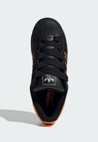 Baskets Adidas noires avec des rayures orange et un accent au talon, bout de chaussure texturé, et lacets noirs, vues du dessus sur un fond blanc.
