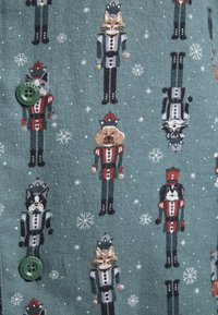 Green fabric featuring whimsical nutcracker patterns with animal figures, snowflakes, and green button detail. Soft texture, playful design.