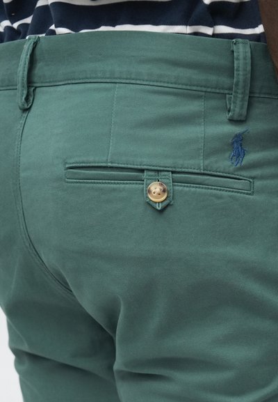 Πράσινο βαμβακερό παντελόνι με πίσω τσέπη που κλείνει με κουμπί και μικρό μπλε κεντητό λογότυπο. Λεία υφή και κομψή γραμμή.