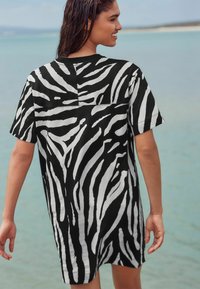 Robe à manches courtes rayée noir et blanc avec une coupe ample, un encolure ronde et une texture douce, portée par une personne de dos.