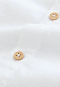 Tessuto di lino bianco con una texture liscia, caratterizzato da un bottone di legno con quattro fori, cucito sul materiale vicino al centro.