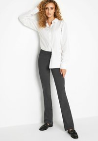 Camisa blanca de manga larga con botones y una ligera textura, combinada con pantalones rectos de color gris oscuro. Zapatillas negras de tipo slip-on completan el atuendo.