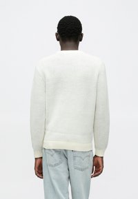 Lichtgekleurde gebreide trui met een gestructureerde afwerking, uitgevoerd met lange mouwen en een geribde zoom, gecombineerd met lichtblauwe spijkerbroek.