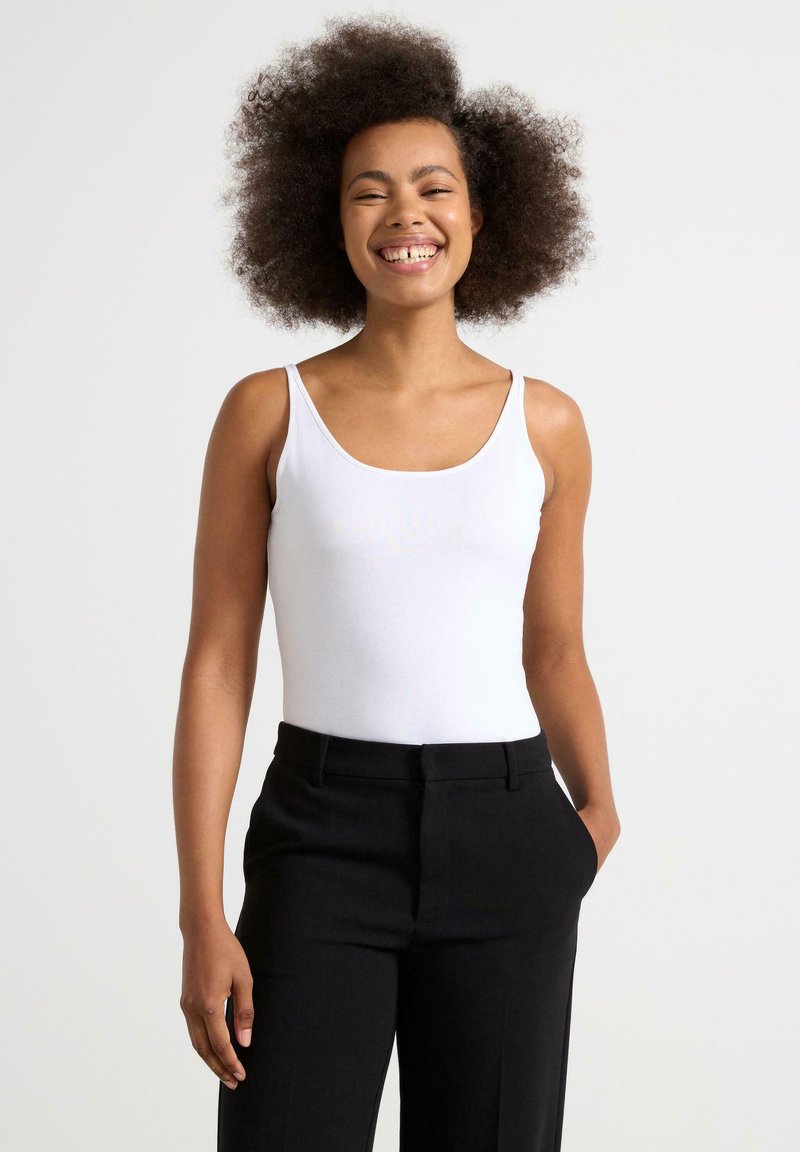 Hvid ærmeløs bodysuit med en glat tekstur, ledsaget af sorte skræddersyede bukser. Outfittet har en rund halsudskæring og slim fit.