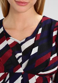 Monivärinen paita, jossa on punaisia, sinisiä ja valkoisia vinoraitoja, V-pääntie ja teksturoitu kangas. Rentoa muotoilua, joka sopii erilaisiin tilaisuuksiin.