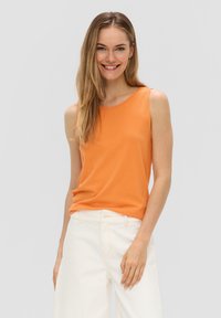 Oranje mouwloze tanktop van zacht materiaal, met een ronde halslijn. Gecombineerd met witte hoge taillebroeken in een ontspannen pasvorm.