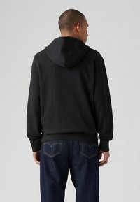 Black hooded sweatshirt with a relaxed fit, ribbed cuffs, and hem. Features a smooth texture and visible stitching around the pocket area.