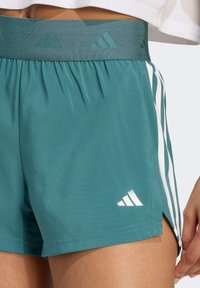 Türkise Sportshorts mit einem strukturierten Bund, seitlichen weißen Streifen und einem weißen Adidas-Logo nahe dem Saum. Glattes Material und kurze Länge.