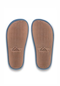 Hnědé gumové podešve s texturovaným vlnovým vzorem, obroubené modrou barvou, se značkovým logem Quiksilver vyraženým uprostřed.