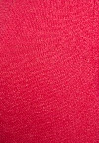 Gros plan sur un tissu tricoté rouge texturé montrant un fin motif tissé et une surface de matériau douce.