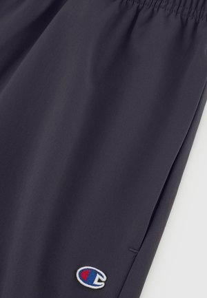 Pantalones cortos deportivos de color gris oscuro, confeccionados en una tela suave, con una cintura elástica y un pequeño logotipo bordado en azul, rojo y blanco.