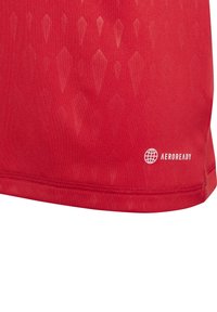 T-shirt de sport rouge avec un motif texturé en diamants, fabriqué en tissu respirant. Présente le logo "AEROREADY" près de l'ourlet.