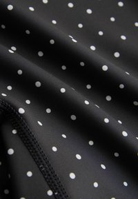 Tissu noir avec de petits pois blancs uniformément espacés et une couture visible le long d'une couture incurvée.