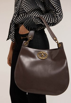 Braune Lederhandtasche mit glatter Oberfläche, runder Form, goldenen Metallakzenten und einem Schultergurt, präsentiert neben einem gemusterten Hemd.