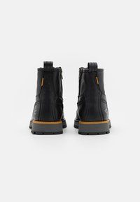 Black leather ankle boots with grey rubber soles, featuring yellow accents and zippers. Reinforced stitching along the sides.