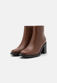 Botas de tobillo de imitación de cuero marrón con punta redonda, tacón cuadrado y superficie lisa, con un detalle de cremallera lateral.
