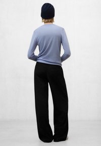 Top de manga larga azul claro, de textura suave, combinado con pantalones negros de pierna ancha. El modelo lleva un gorro oscuro, visto desde atrás contra un fondo neutro.