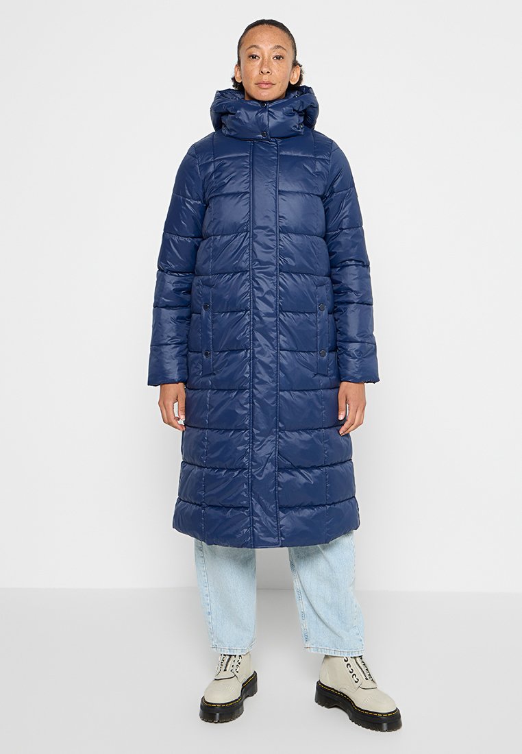 Cappotto imbottito blu navy con colletto alto, maniche lunghe e tasche con bottone. Presenta una texture trapuntata e un design sotto il ginocchio.