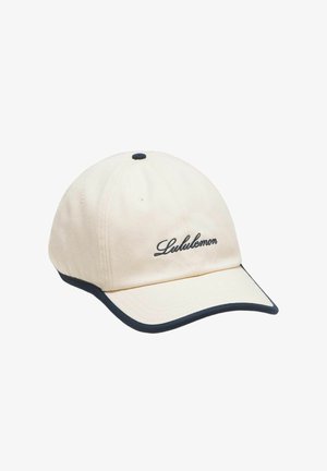 Beżowa czapka baseballowa z czarną lamówką i czarnym kursywowym logo Lululemon z przodu, pokazana na białym tle.