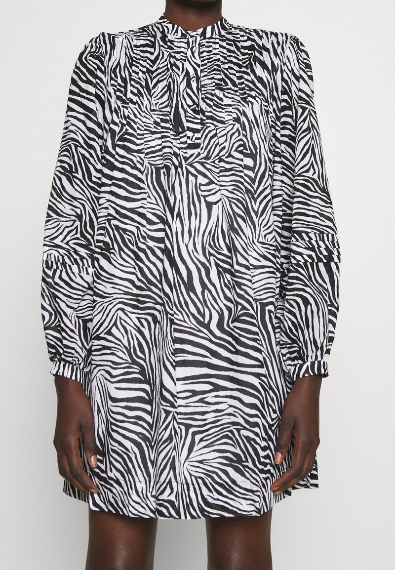 Abito a stampa zebra in bianco e nero con maniche lunghe e arricciate e collo alto. Tessuto leggero, taglio dritto e dettagli plissettati.