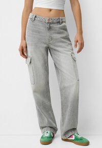 Vaqueros cargo de color gris claro con un corte holgado, que cuentan con bolsillos laterales y cierre de botones. Combinados con zapatillas verdes y rosas.