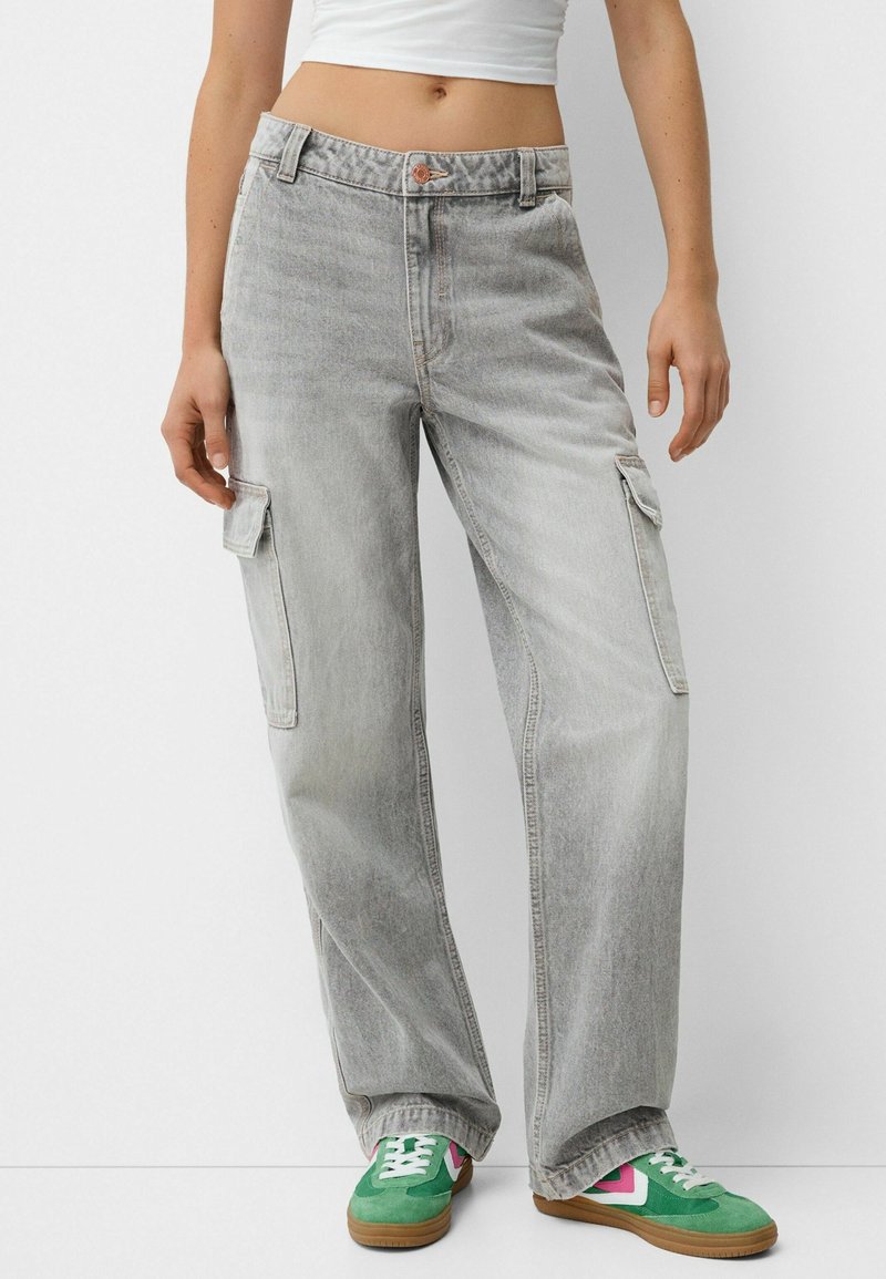 Vaqueros cargo de color gris claro con un corte holgado, que cuentan con bolsillos laterales y cierre de botones. Combinados con zapatillas verdes y rosas.