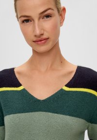 Strickpullover mit V-Ausschnitt, der horizontale Streifen in dunkelblau, grün, hellgrün und gelb aufweist. Die Textur wirkt weich und flauschig.