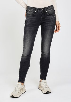 Schwarz Slim-Fit-Jeans mit einer ausgewaschenen Optik, fünf Taschen-Design und silbernen Hardware-Details, kombiniert mit hellen Sneakers.