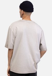 Lys grå oversized T-skjorte med korte ermer, rund hals og en jevn tekstur. Har en liten sideetikett og avslappet silhuett.