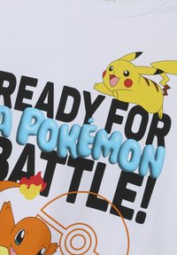 Camiseta blanca con gráficos coloridos de Pikachu y Charmander, con un texto en negrita negro que dice "¡LISTO PARA UNA BATALLA POKÉMON!" en azul.