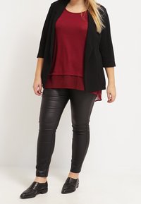 Svart kavaj över en vinröd lagerblus, kombinerad med svarta byxor i konstläder och svarta loafers, med en stilren design och slim fit.