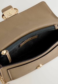 Intérieur d'un sac à main en cuir beige avec une doublure en tissu noir. Comprend un compartiment zippé et des accents en métal doré.