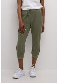 Olijfgroene, lichte joggingbroek met elastische boorden en een tailleband met trekkoord. Gekleed met witte sneakers voor casual comfort.