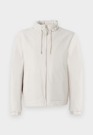 Chaqueta beige clara hecha de una tela suave, con cierre de cremallera, cordones ajustables en el cuello y puños elásticos.