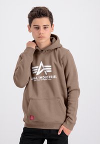 Felpa marrone con tasca frontale e logo "Alpha Industries" bianco. Presenta un cappuccio con coulisse e polsini a costine. Tessuto testurizzato.