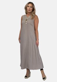 Beżowa, bezrękawnikowa sukienka maxi o prostym kroju, z pionowymi akcentami w postaci guzików i lekkim materiałem. Noszona z espadrylami na koturnie.