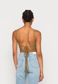 Bralette lavorato a maglia verde oliva con spalline regolabili e una schiena annodata. Abbinato a jeans in denim azzurro chiaro a vita alta.