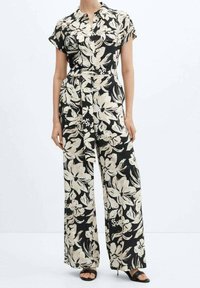 Mono floral en negro y crema con manga corta, cuello tipo camisa, piernas anchas y cintura ceñida. Presenta un detalle atado en la cintura.