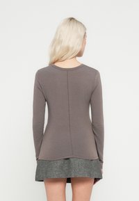 Bluză maro cu mâneci lungi, gât rotund, croială strâmtă și o cusătură dreaptă pe spate, asortată cu o fustă gri texturată.