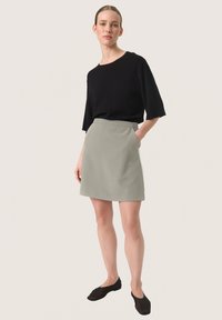Top scurt negru cu mânecă scurtă, asociat cu o fustă mini gri deschis cu buzunare. Modelul poartă încălțăminte tip slip-on negre. Textura materialului este fină.
