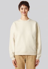 Felpa oversize color crema con scollatura rotonda, polsini e orlo a coste, caratterizzata da una texture liscia e una vestibilità comoda.