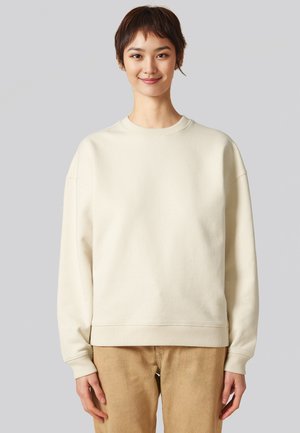 Sweatshirt surdimensionné de couleur crème avec un col rond, des poignets et un ourlet côtelés, présentant une texture lisse et une coupe décontractée.