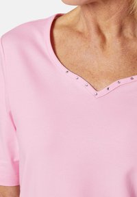 Rosa Kurzarm-T-Shirt mit V-Ausschnitt, verziert mit kleinen dekorativen R rhinestones entlang des Randes, aus weichem, glattem Stoff gefertigt.